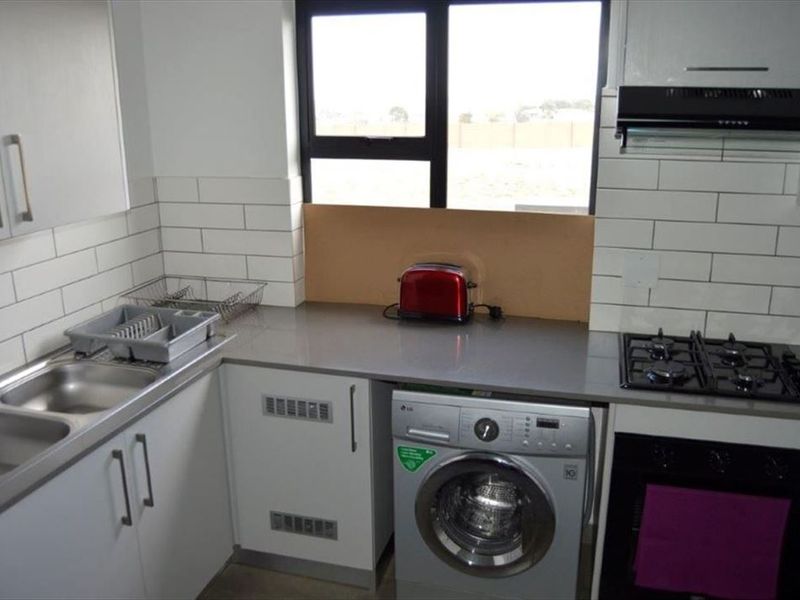 Compact kitchen featuring quartz countertops, subway tile backsplash, gas hob, built-in oven, and integrated laundry plumbing.