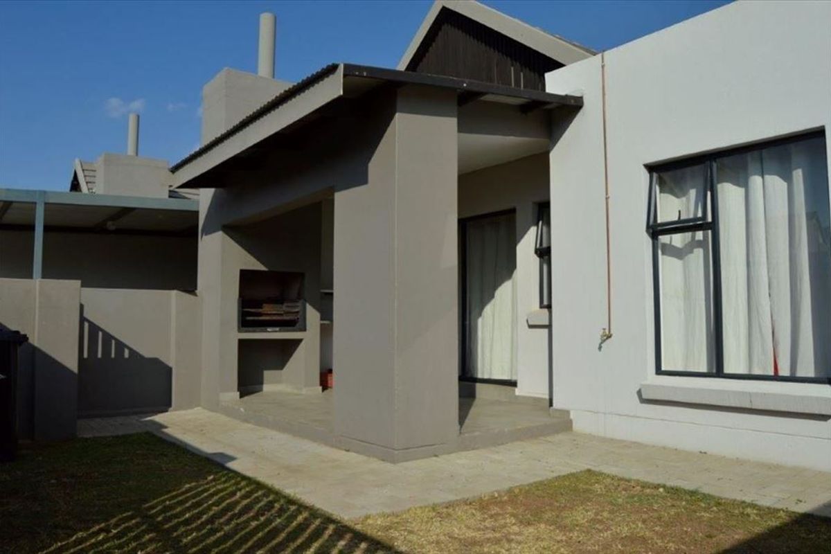 A covered patio area featuring a built-in braai, paved flooring, and direct access to the garden through sliding doors.