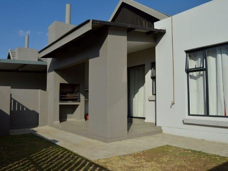 A covered patio area featuring a built-in braai, paved flooring, and direct access to the garden through sliding doors.