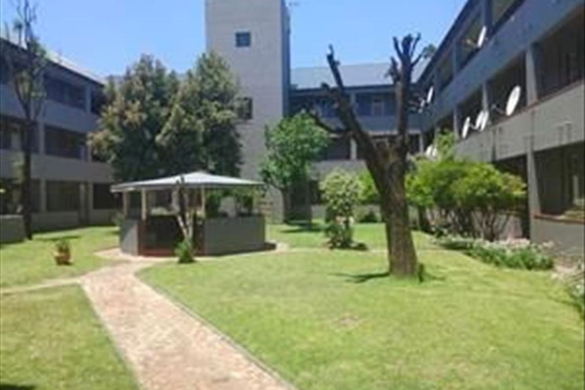 A communal garden area within an apartment complex featuring a paved walkway, manicured lawn, and a covered gazebo structure.