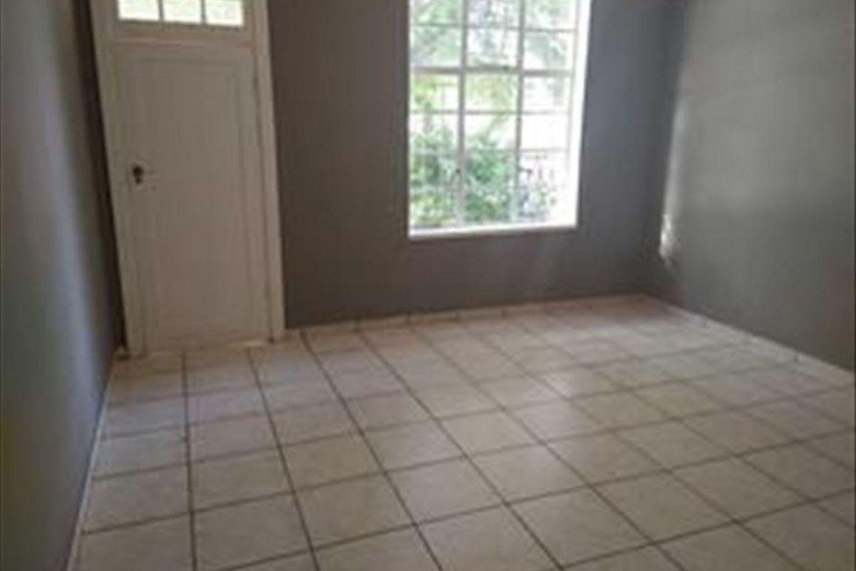 An empty bedroom featuring tiled flooring, a large window with natural light, and a classic door with a transom window.