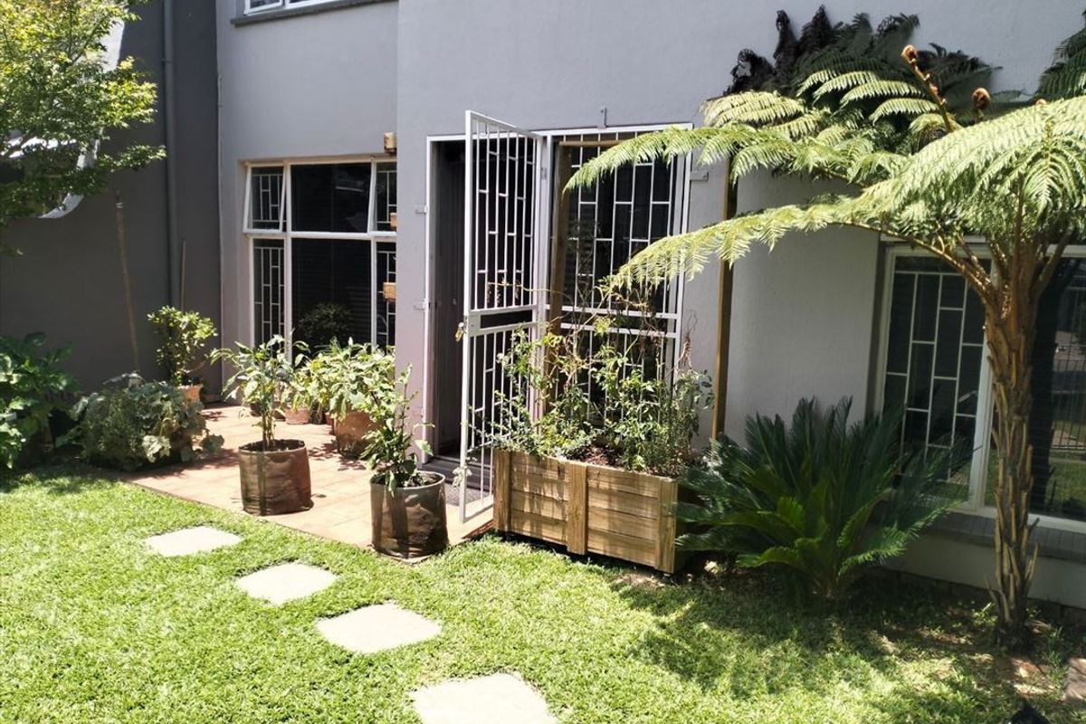 Rear exterior view of the townhouse featuring a small tiled patio, security gates, and a landscaped garden area with stepping stones.