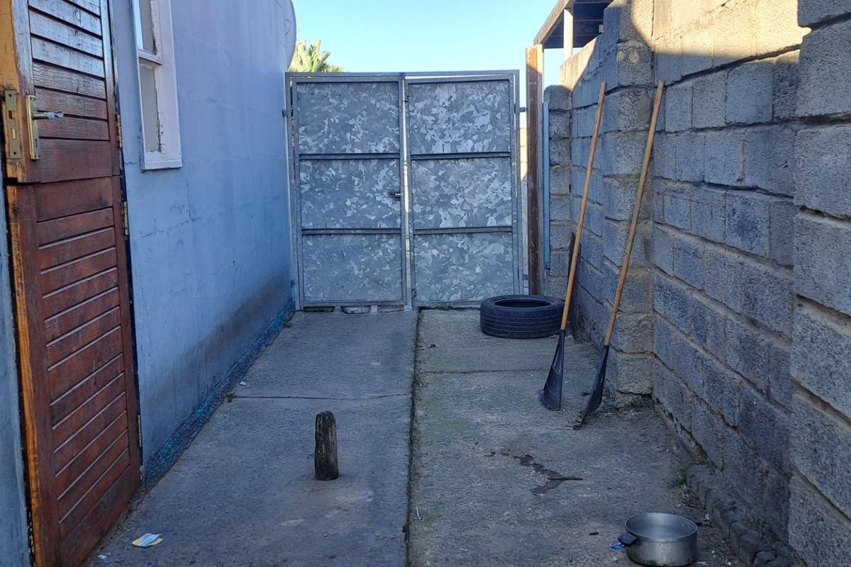 A narrow side passage featuring concrete paving, a cinder block boundary wall, and a galvanized steel gate leading to the rear of the property.