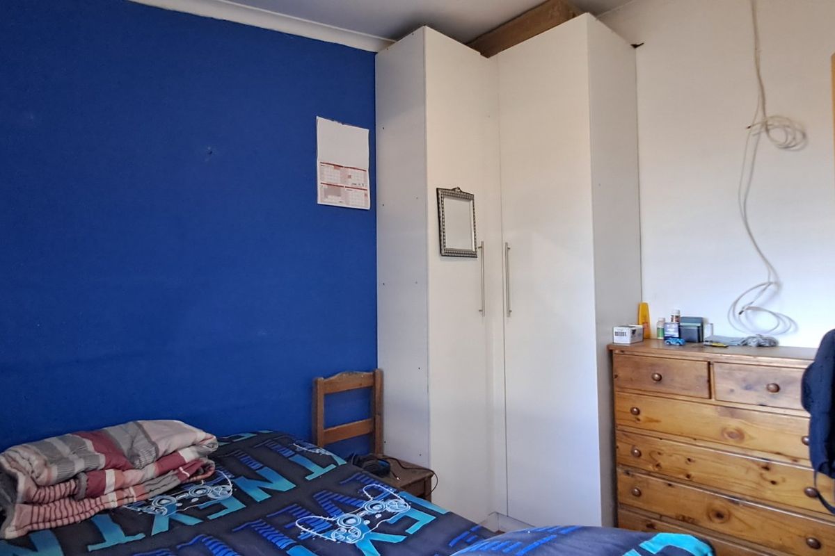 A bedroom featuring a built-in wardrobe and blue accent wall, requiring cosmetic updates and electrical cable management.
