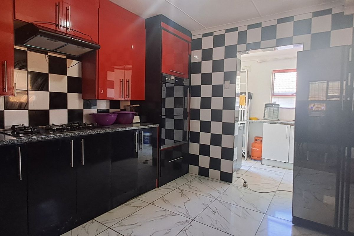 Kitchen featuring high-gloss red and black cabinetry, a gas hob with extractor, built-in oven, and a distinctive black and white checkered tiled splashback.