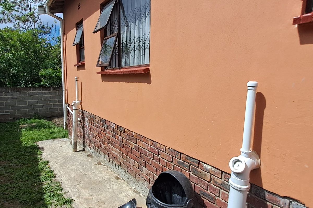 Side exterior view of the house featuring brick base, painted walls, security bars on windows, and exposed plumbing infrastructure.