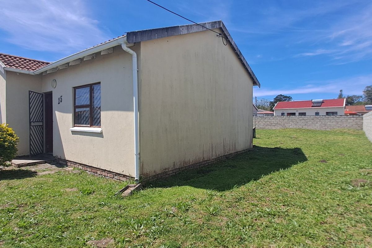 Rear view of the property featuring a private garden enclosed by concrete block boundary walls and a tiled roof structure.