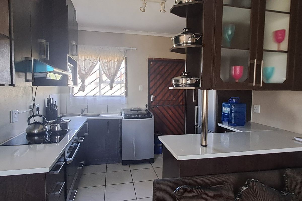 A functional kitchen featuring dark wood cabinetry, white stone countertops, a built-in hob with extractor fan, and a convenient breakfast bar area.