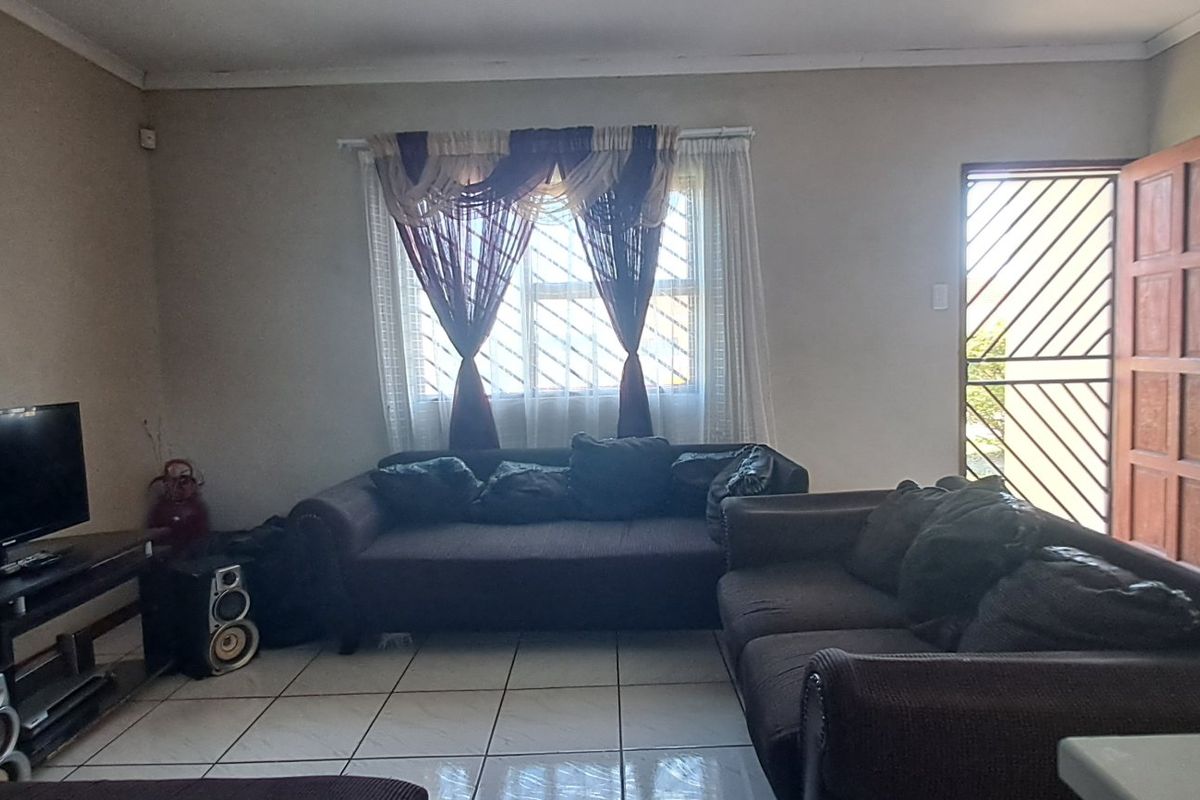 A functional living room featuring tiled flooring, a secure entrance door with a security gate, and natural light through the window.