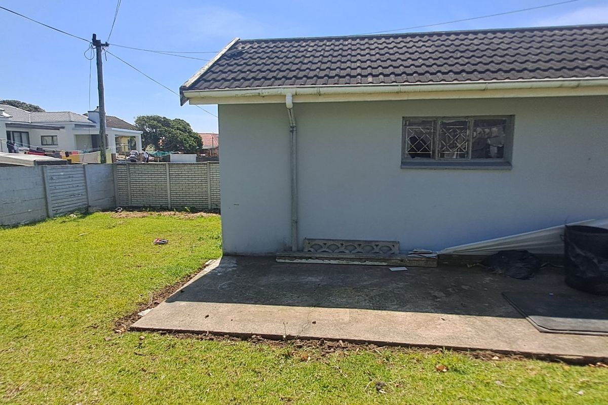Rear exterior view of the property featuring a concrete patio area, a small lawn, and a precast concrete boundary wall.