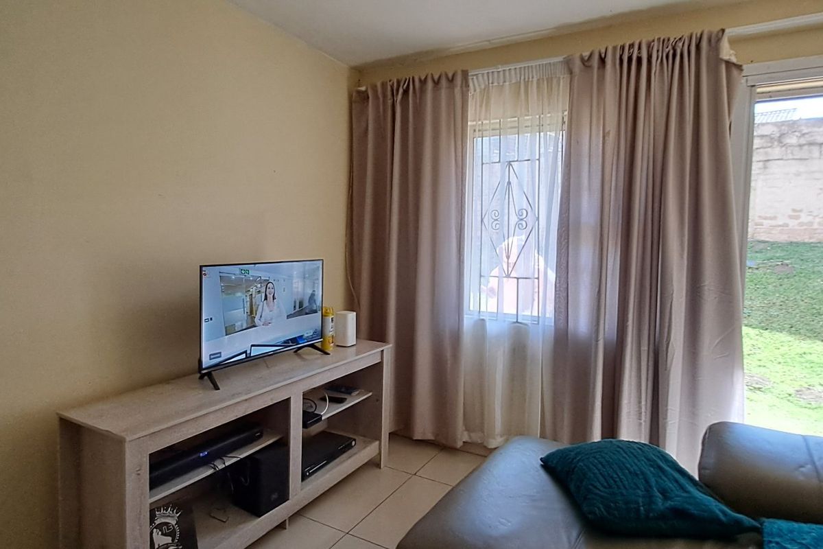 A living room featuring tiled flooring, a security gate, and a sliding door providing access to the outdoor area.