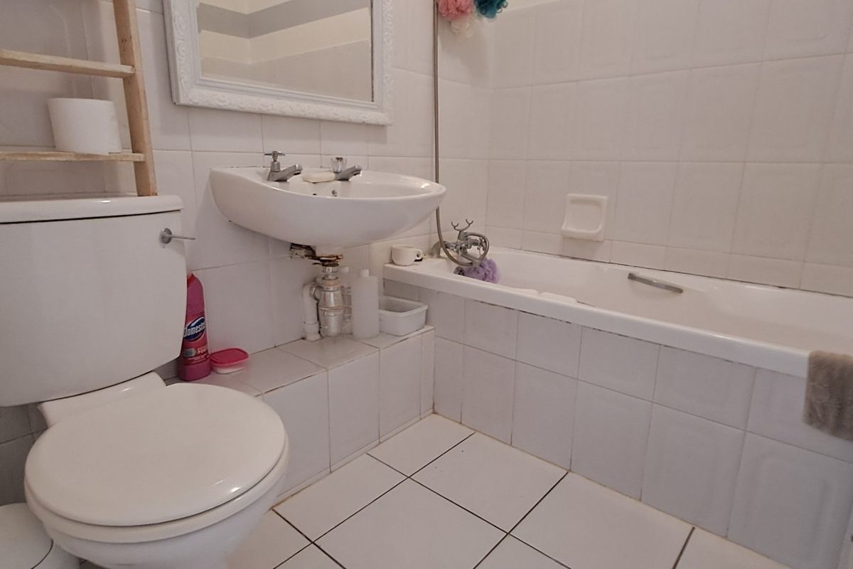 A functional bathroom featuring a standard bathtub, pedestal washbasin, and toilet with white ceramic wall and floor tiling.