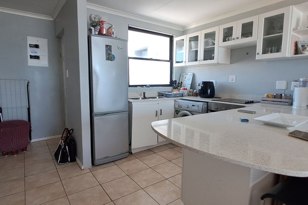 A functional kitchen featuring stone countertops, built-in cabinetry, a hob, and an oven, with tiled flooring and a breakfast bar area.