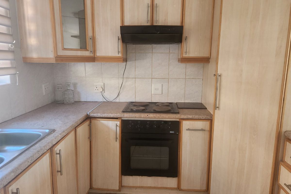 Compact kitchen featuring light wood-finish cabinetry, laminate countertops, a built-in oven, electric hob, and extractor fan with tiled splashback.