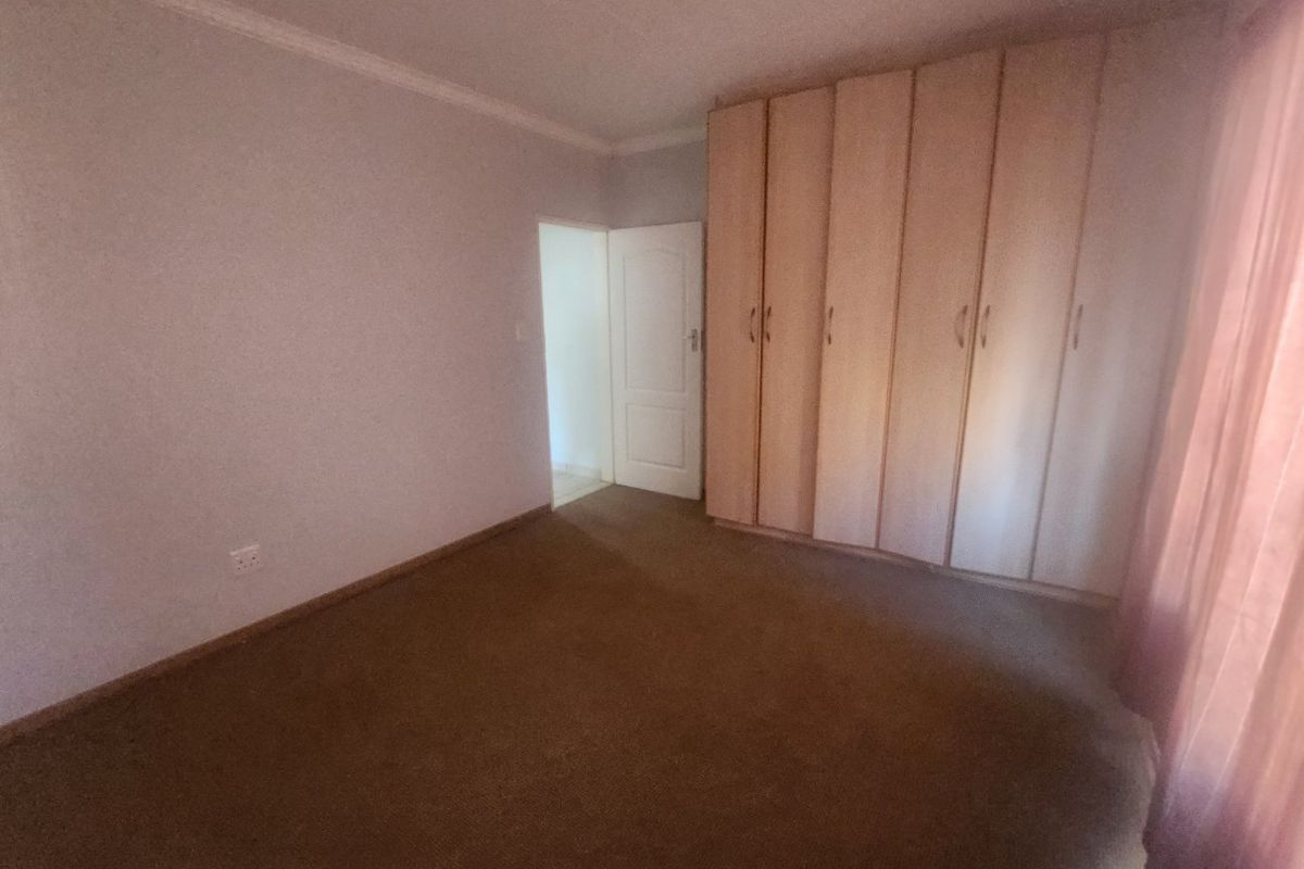 A bedroom featuring built-in wooden cupboards, carpeted flooring, and neutral wall finishes, offering a functional and well-proportioned living space.