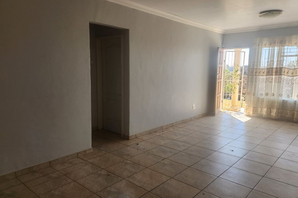 An empty living room featuring tiled flooring, a doorway leading to an interior space, and a door providing access to the exterior.