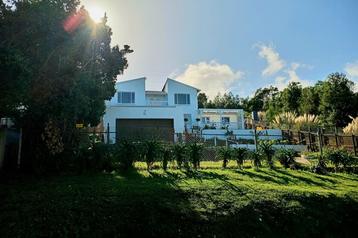 Rear view of a two-story house featuring a double garage, upper-level balcony, and a covered patio area overlooking a landscaped garden.