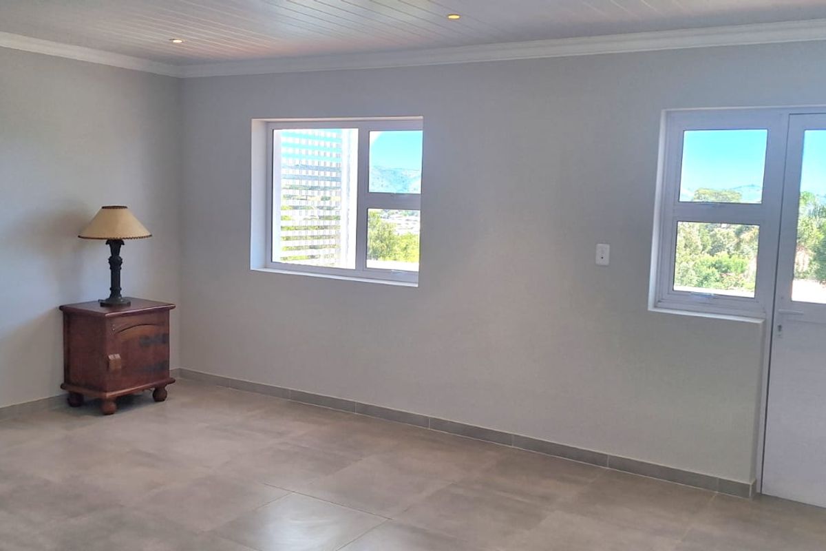 A bright, empty living area featuring neutral tiled flooring, recessed ceiling lighting, and large windows providing natural light and outdoor views.