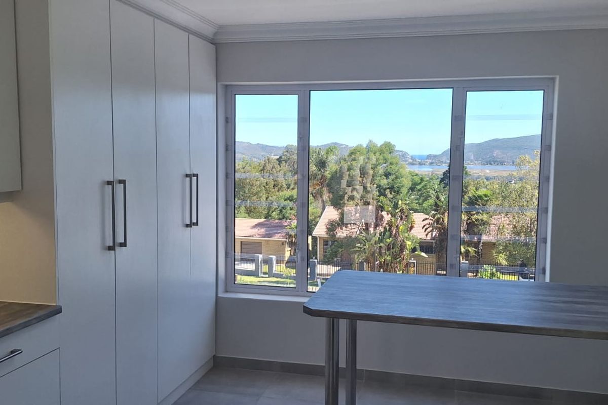 Modern kitchen area featuring sleek built-in cabinetry, laminate countertops, and a breakfast bar, complemented by a large window offering scenic landscape views.