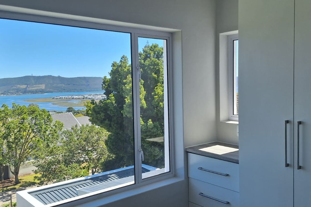 A bright bedroom featuring built-in cupboards, a vanity unit, and large windows offering expansive views of the estuary and surrounding landscape.