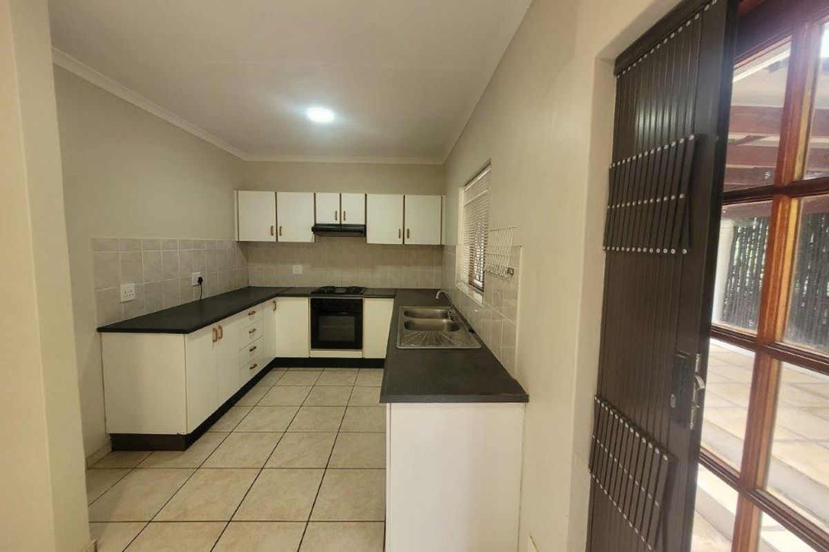 A functional kitchen featuring white cabinetry, dark countertops, a built-in oven and hob, and tiled flooring, with direct access to an outdoor patio area.