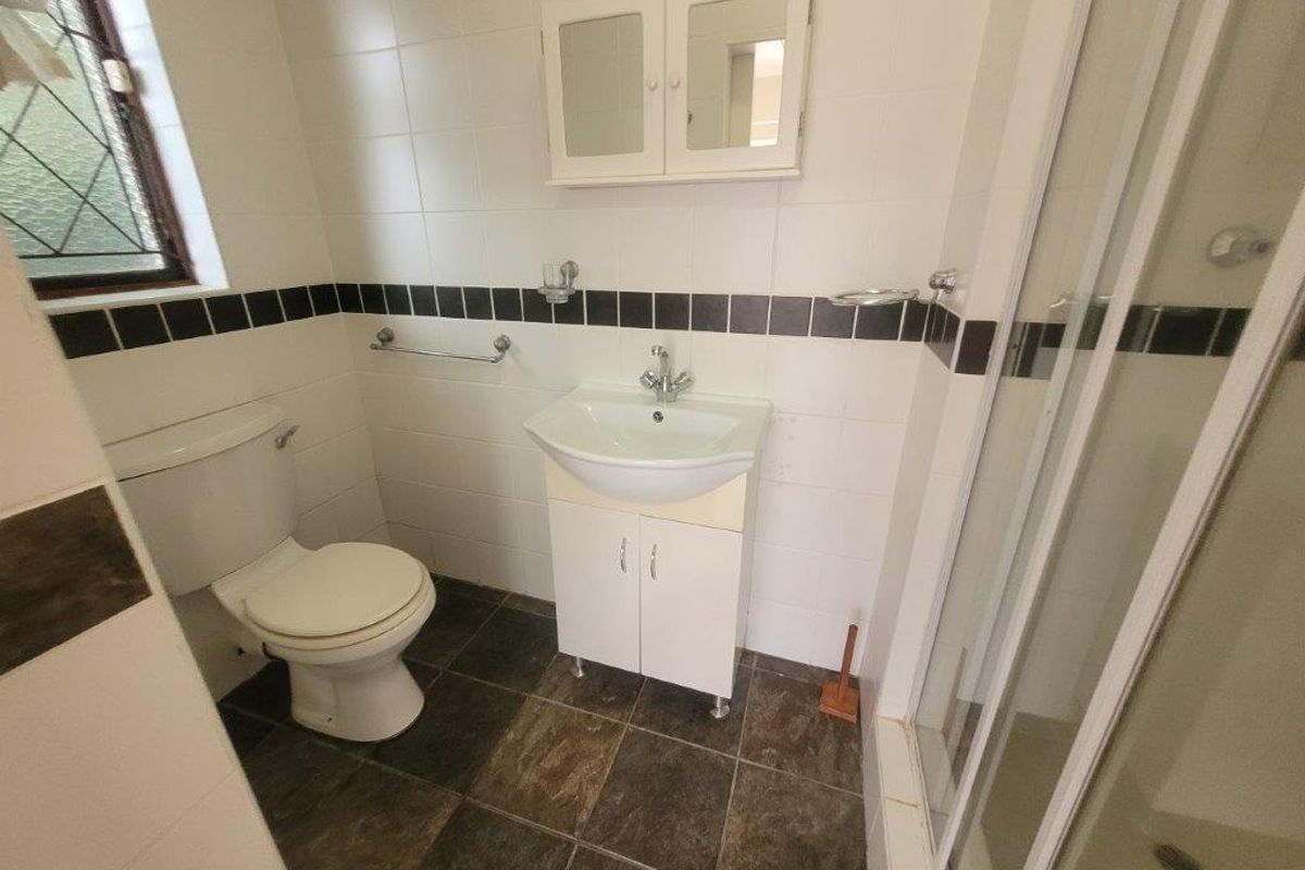 A functional bathroom featuring a shower enclosure, vanity basin, and toilet with neutral wall tiling and dark floor tiles.