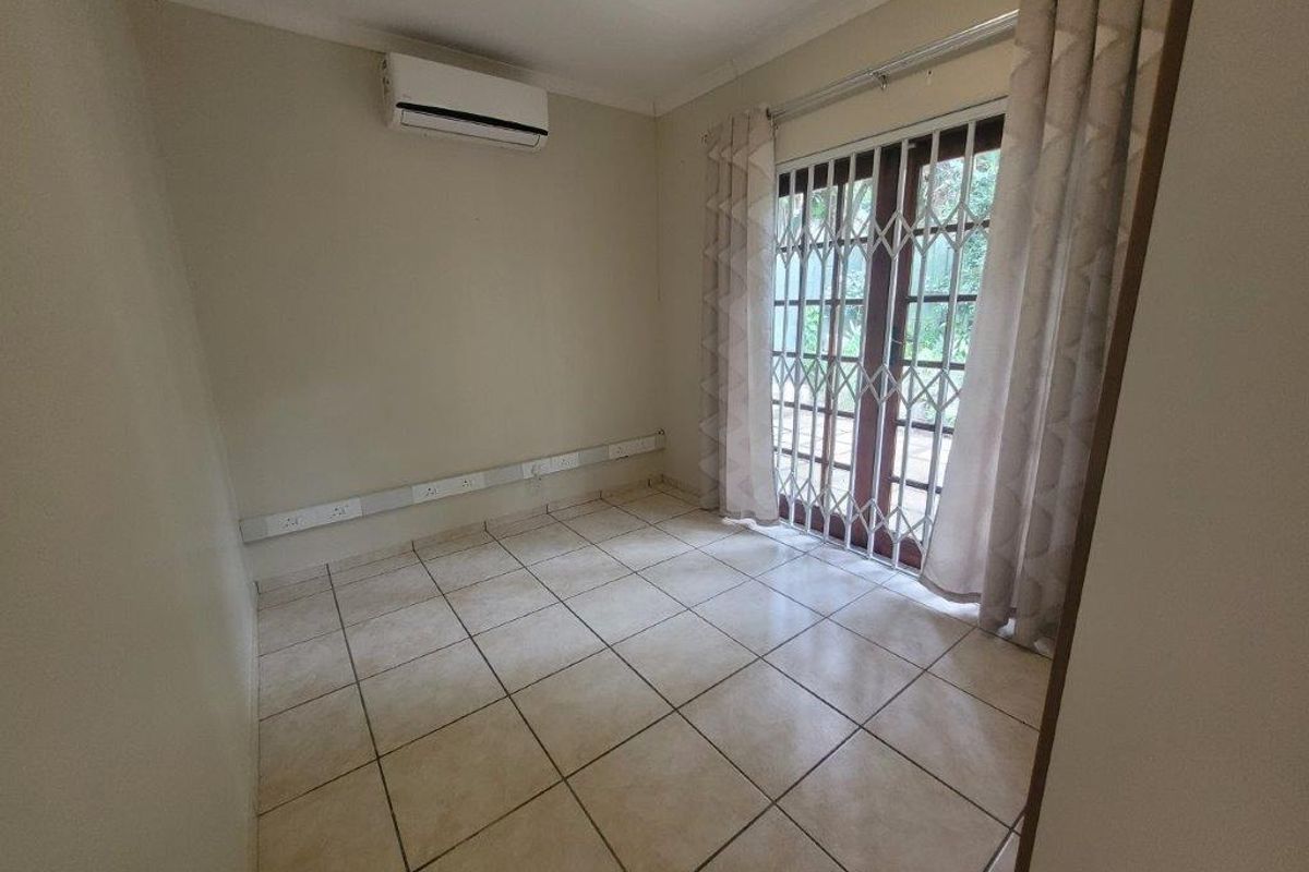 An empty bedroom featuring tiled flooring, a wall-mounted air conditioning unit, and a sliding glass door with a security gate leading outdoors.