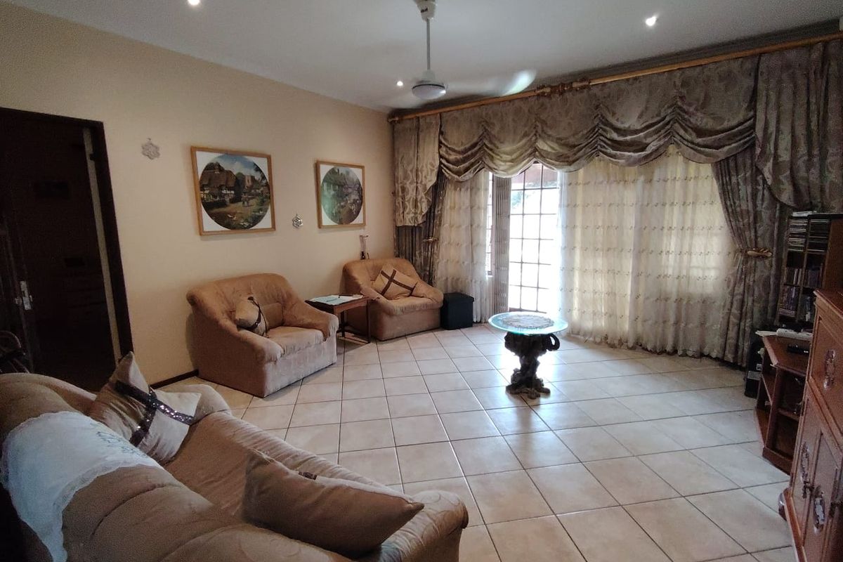 A spacious living room featuring neutral tiled flooring, recessed lighting, a ceiling fan, and large sliding glass doors providing access to the outdoor area.