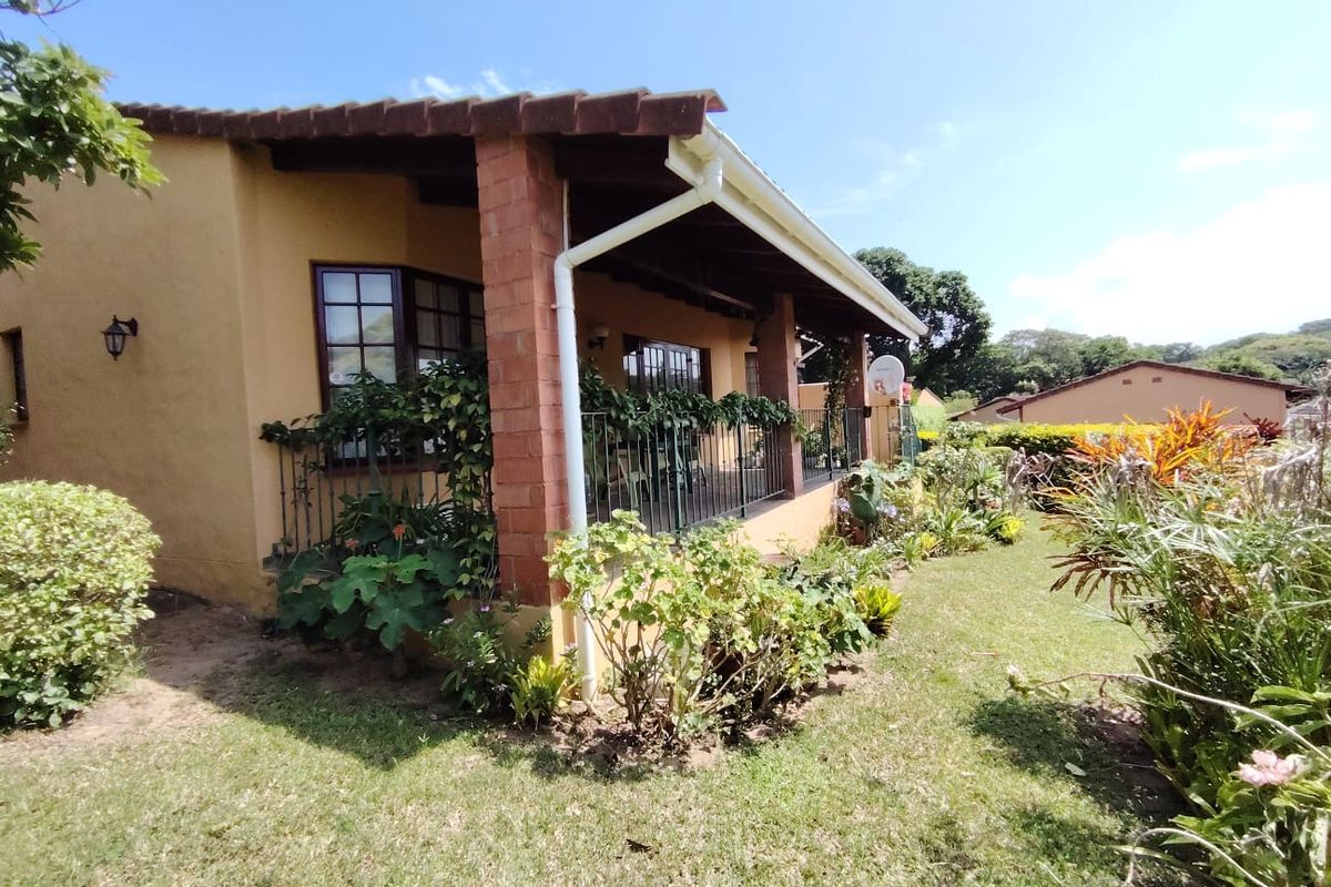 Rear view of the townhouse featuring a covered patio with brick pillars, tiled roof, and established garden surroundings.