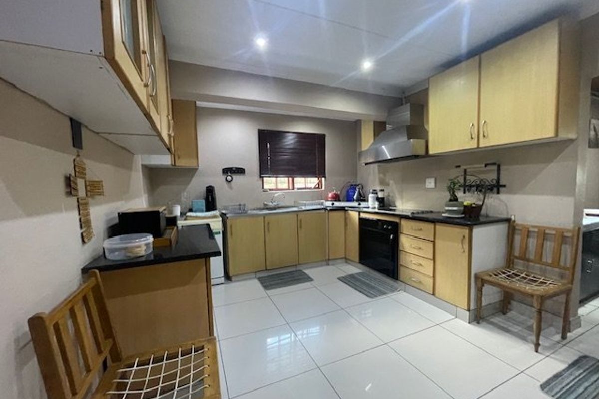 A functional kitchen featuring light wood cabinetry, granite countertops, stainless steel extractor fan, built-in oven, and polished ceramic floor tiles.