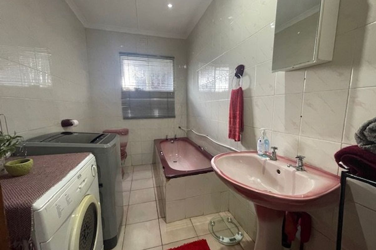 A functional bathroom featuring tiled walls and flooring, a pedestal basin, and a built-in bathtub, offering potential for modernization and cosmetic updates.