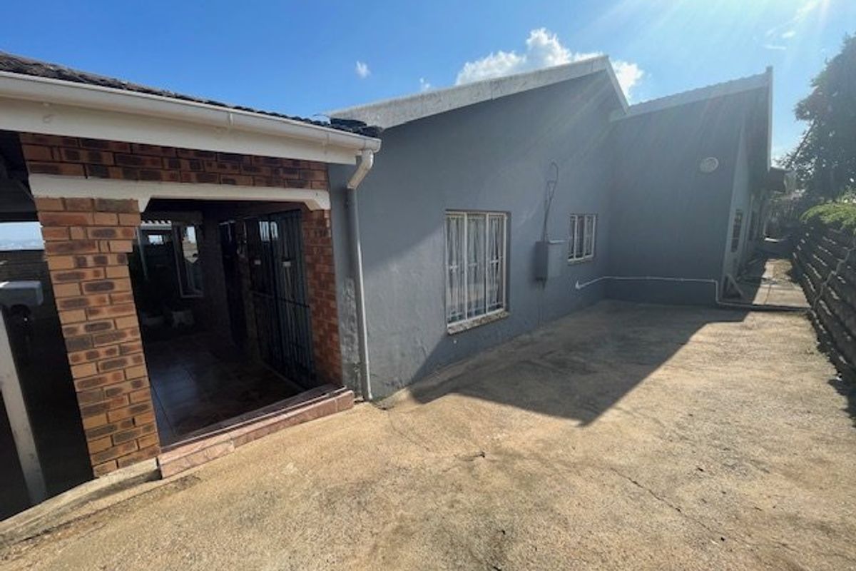 Rear exterior view of the house featuring a covered patio area with brick pillars, concrete paving, and security gates.