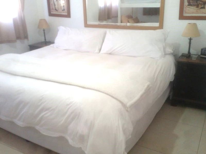 A functional bedroom featuring tiled flooring and a large wall-mounted mirror, providing a neutral space ready for personalization.