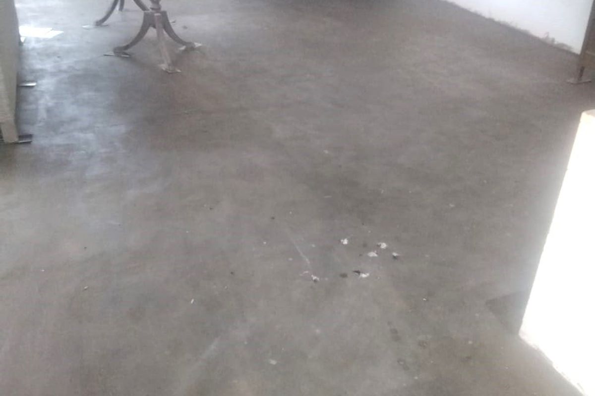 An interior living space featuring raw concrete flooring and a window, currently in need of finishing and renovation to improve the overall aesthetic.