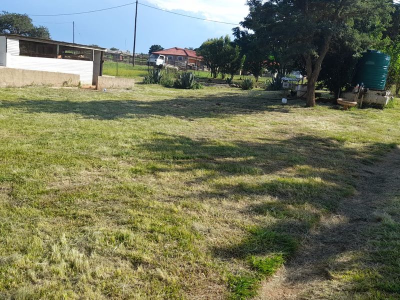 A wide view of the farm garden featuring a large lawn area, a water storage tank, and a small outbuilding structure.