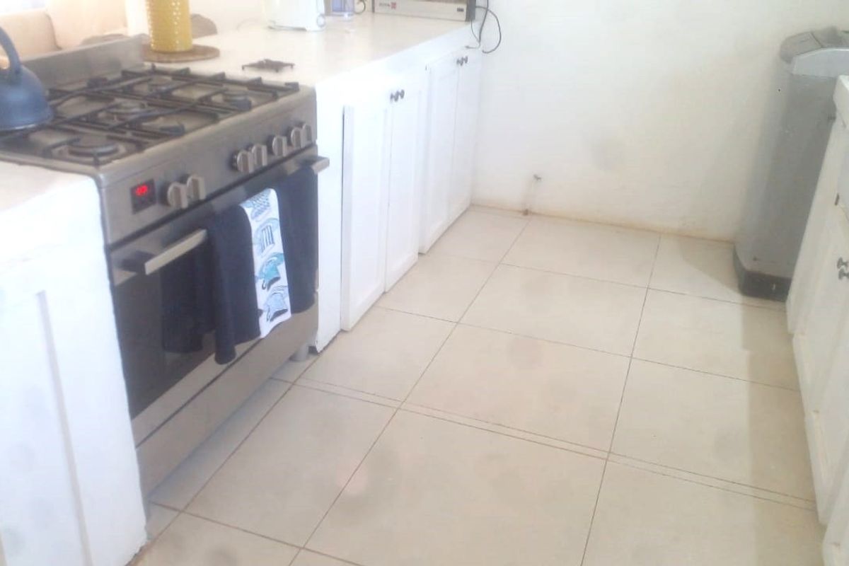 A functional kitchen area featuring built-in cabinetry, a gas stove with oven, and tiled flooring, requiring cosmetic updates to improve its overall condition.