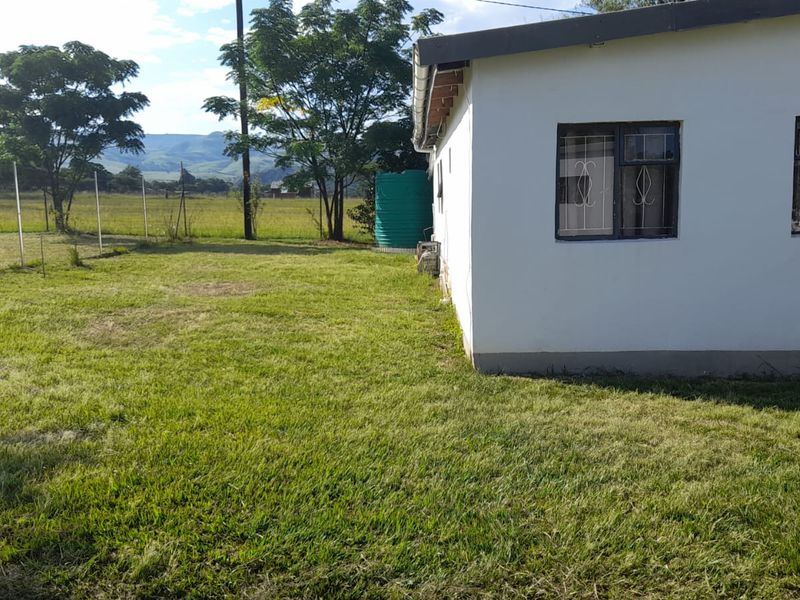 A view of the rear exterior of the farm building, featuring a grass lawn, security bars on windows, and a water tank.