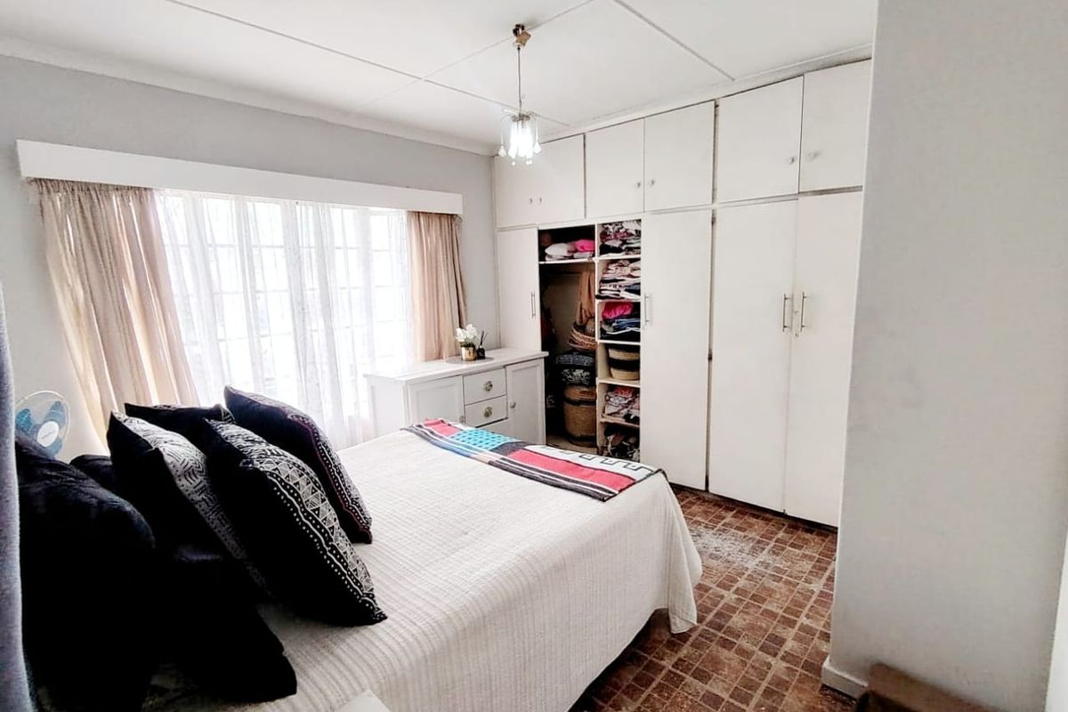 A bedroom featuring built-in cupboards, tiled flooring, and a large window allowing natural light. The room requires cosmetic updates to modernize the finishes.