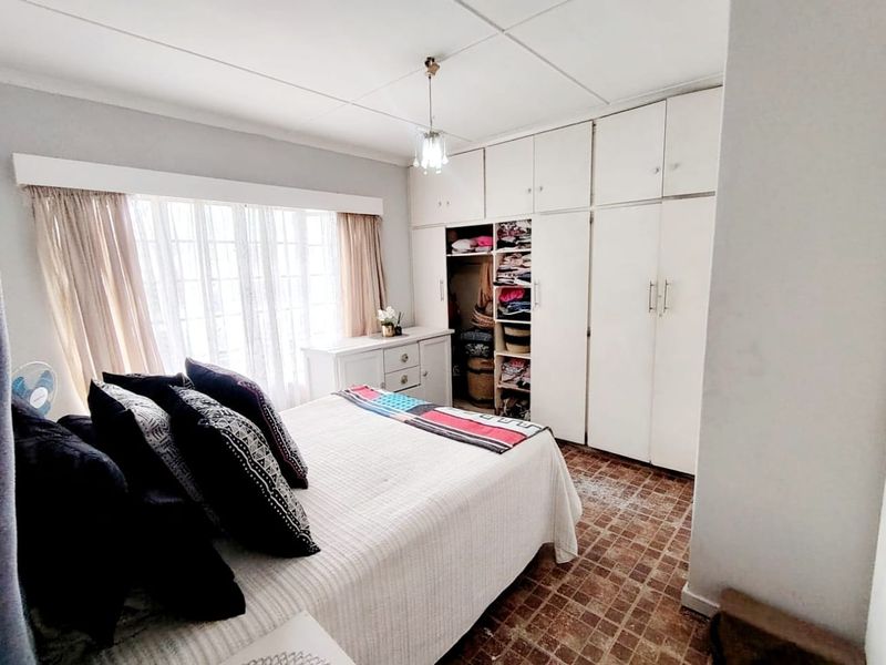 A bedroom featuring built-in cupboards, tiled flooring, and a large window allowing natural light. The room requires cosmetic updates to modernize the finishes.