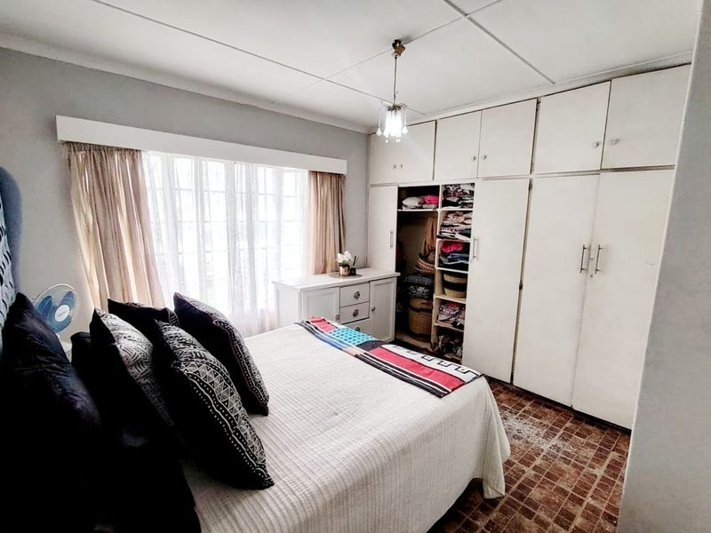 A bedroom featuring built-in floor-to-ceiling cupboards, tiled flooring, and large windows allowing for natural light.