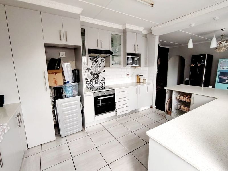 A functional kitchen featuring white cabinetry, stone countertops, a tiled backsplash, and integrated appliances including an oven, hob, and microwave.
