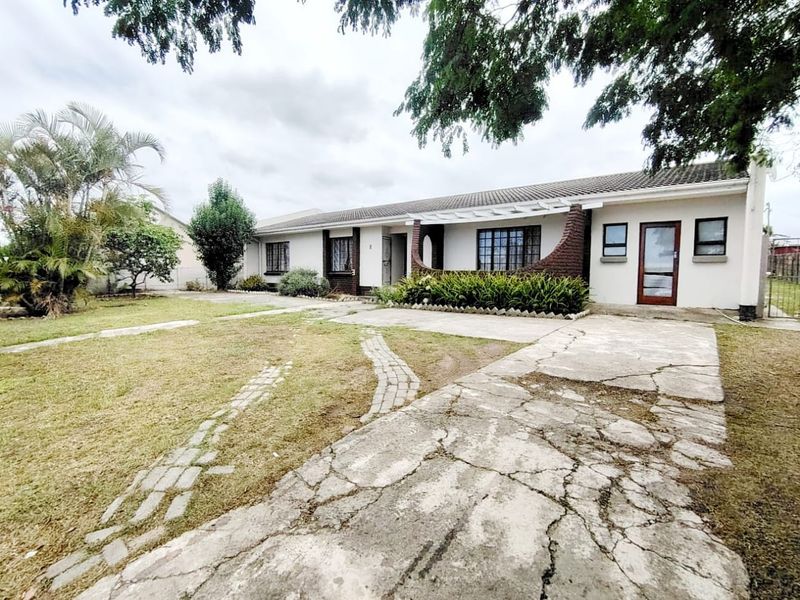 Front view of a single-story house featuring a tiled roof, brick accents, a pergola, and a spacious garden with a concrete driveway.