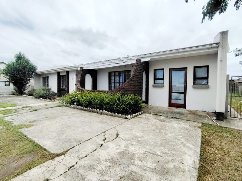 Front elevation of a single-story house featuring a concrete driveway, brick architectural detailing, and a pergola over the entrance area.