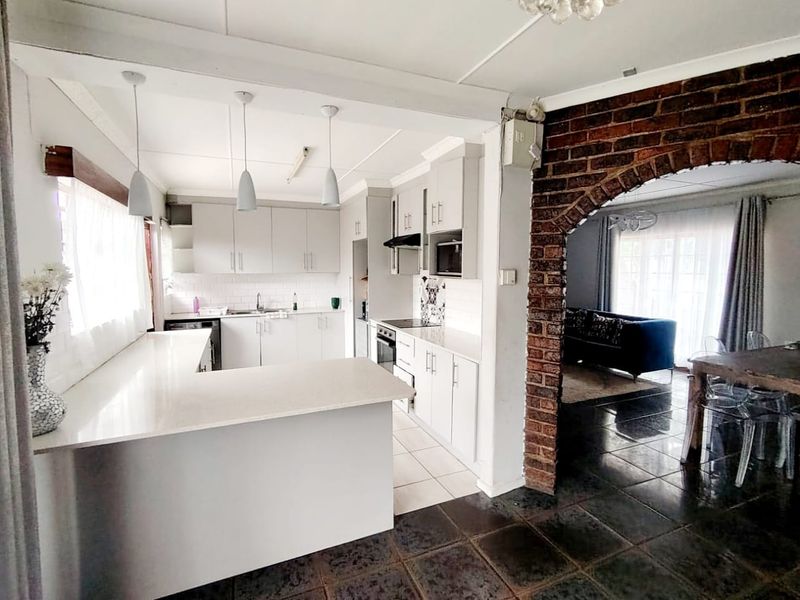 Open plan kitchen featuring modern white cabinetry, stone countertops, and an exposed brick archway leading to the adjacent living and dining area.