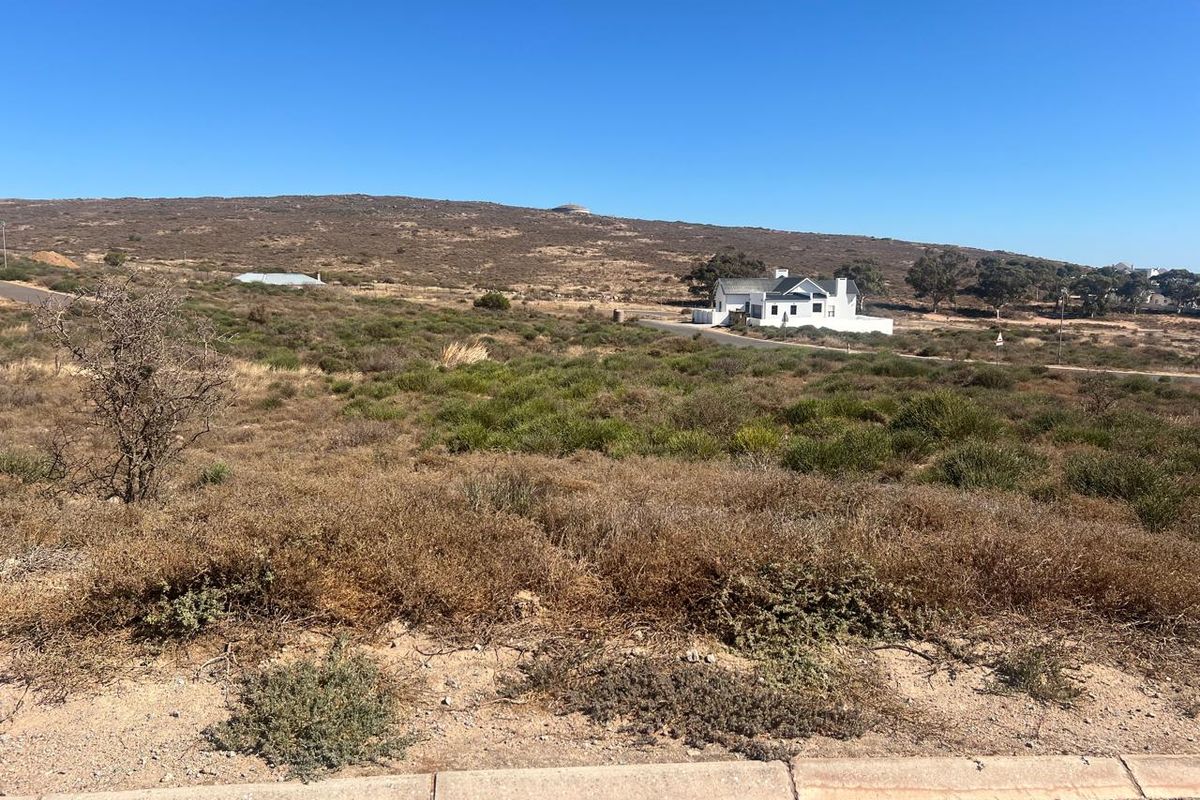 A wide-angle view of a vacant residential plot featuring natural coastal vegetation and surrounding landscape with distant neighboring properties.