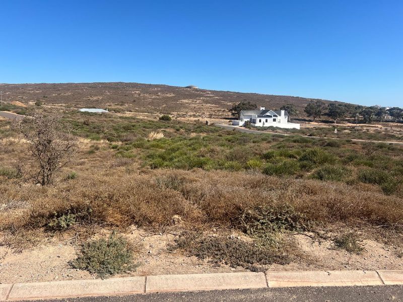A wide-angle view of a vacant residential plot featuring natural coastal vegetation and surrounding landscape with distant neighboring properties.