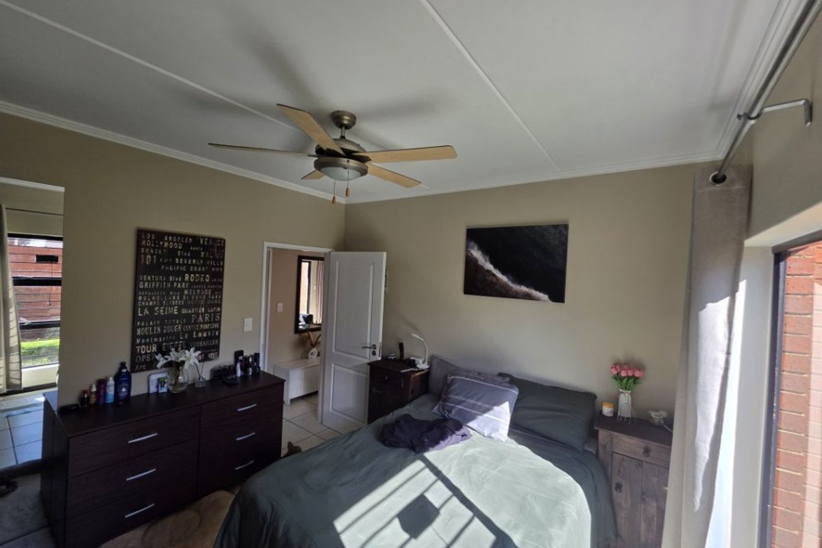 A well-lit bedroom featuring a ceiling fan, tiled flooring, and direct access to an outdoor area through a sliding door.