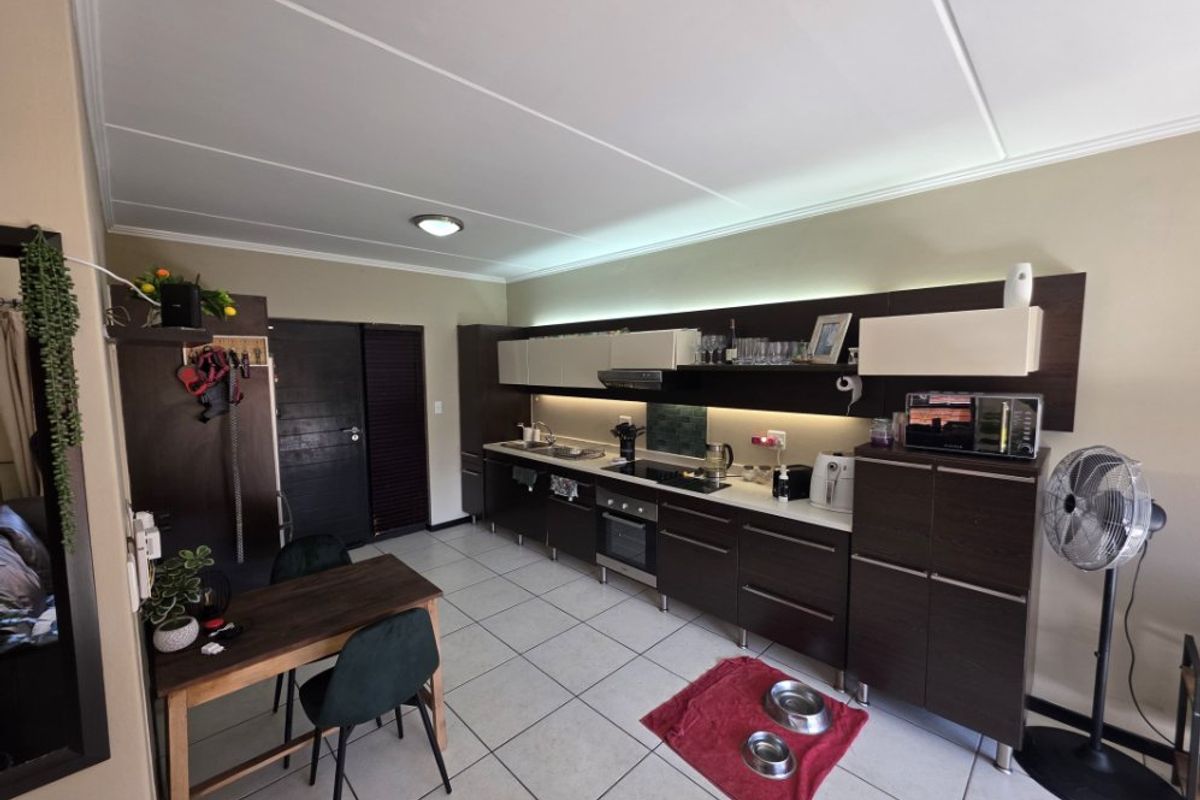 A modern kitchen featuring dark wood cabinetry, integrated oven and hob, under-cabinet lighting, and tiled flooring in an open-plan layout.