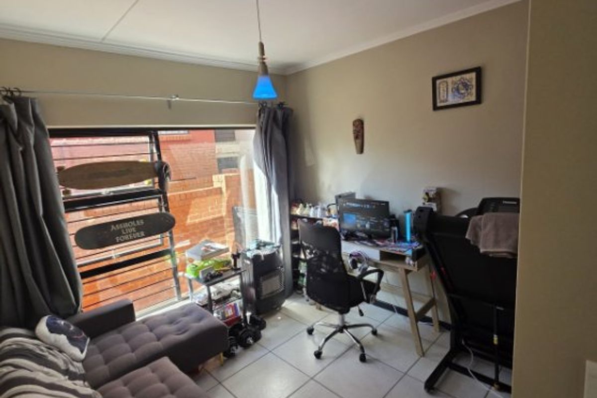 A multi-purpose living space featuring tiled flooring, a large window with security bars, and a pendant light fixture.