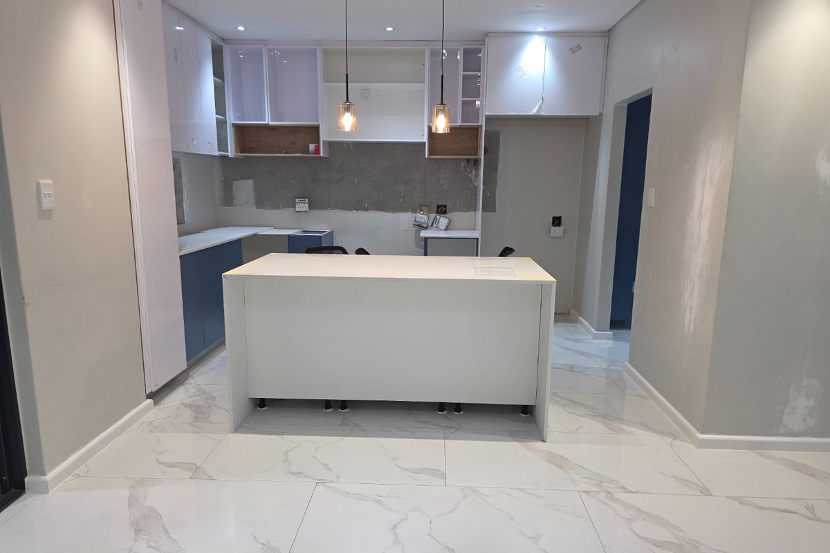 A modern kitchen under construction featuring a central island, white and blue cabinetry, and marble-look floor tiles, awaiting final finishes and backsplash installation.